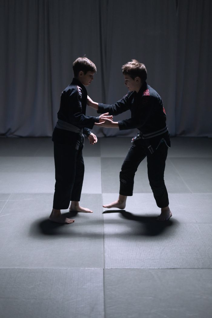 Two young boys sparring in Jiu Jitsu practice, wearing kimonos indoors.