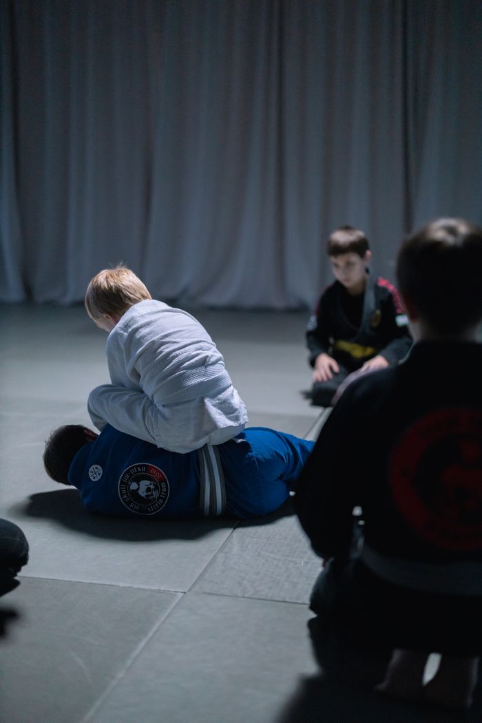 Services Children engage in a Jiu-Jitsu training session indoors, focusing on martial arts techniques.